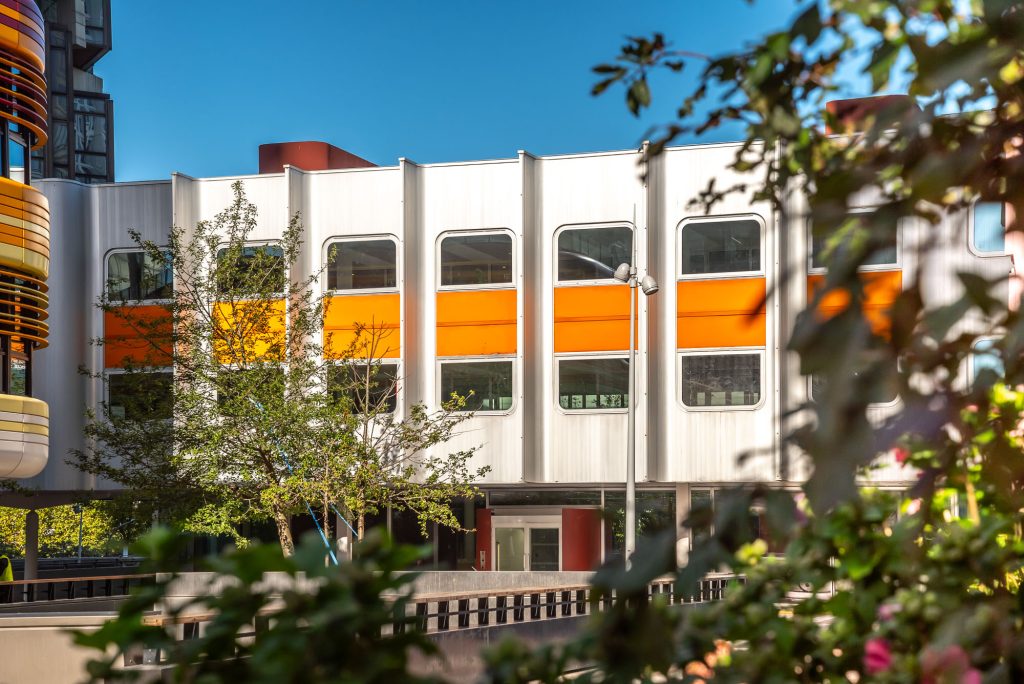 Le bâtiment Orion habillé de métal, de verre et entouré d'un bandeau orange se fond dans la végétation dense de la dalle du Front de Seine Beaugrenelle.