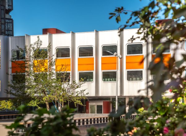 Le bâtiment Orion habillé de métal, de verre et entouré d'un bandeau orange se fond dans la végétation dense de la dalle du Front de Seine Beaugrenelle.